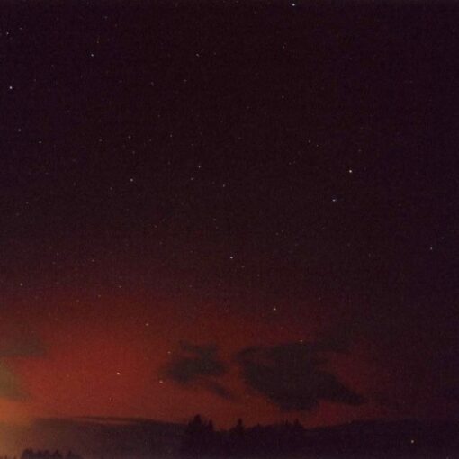 Slika prikazuje rdeč severni sij nad Kamniškimi Alpami in Karavankami, viden iz Vodic.