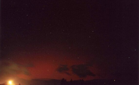 Slika prikazuje rdeč severni sij nad Kamniškimi Alpami in Karavankami, viden iz Vodic.